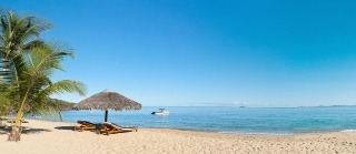 Picture of n idyllic beach scene with desck chairs, parasol, palm trees, guitarand a hat 